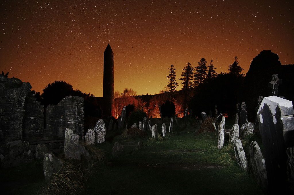 The round tower and graveyard at Glendalough at night, with the glow of Dublin to the north | © Rob Hurson/WikiCommons