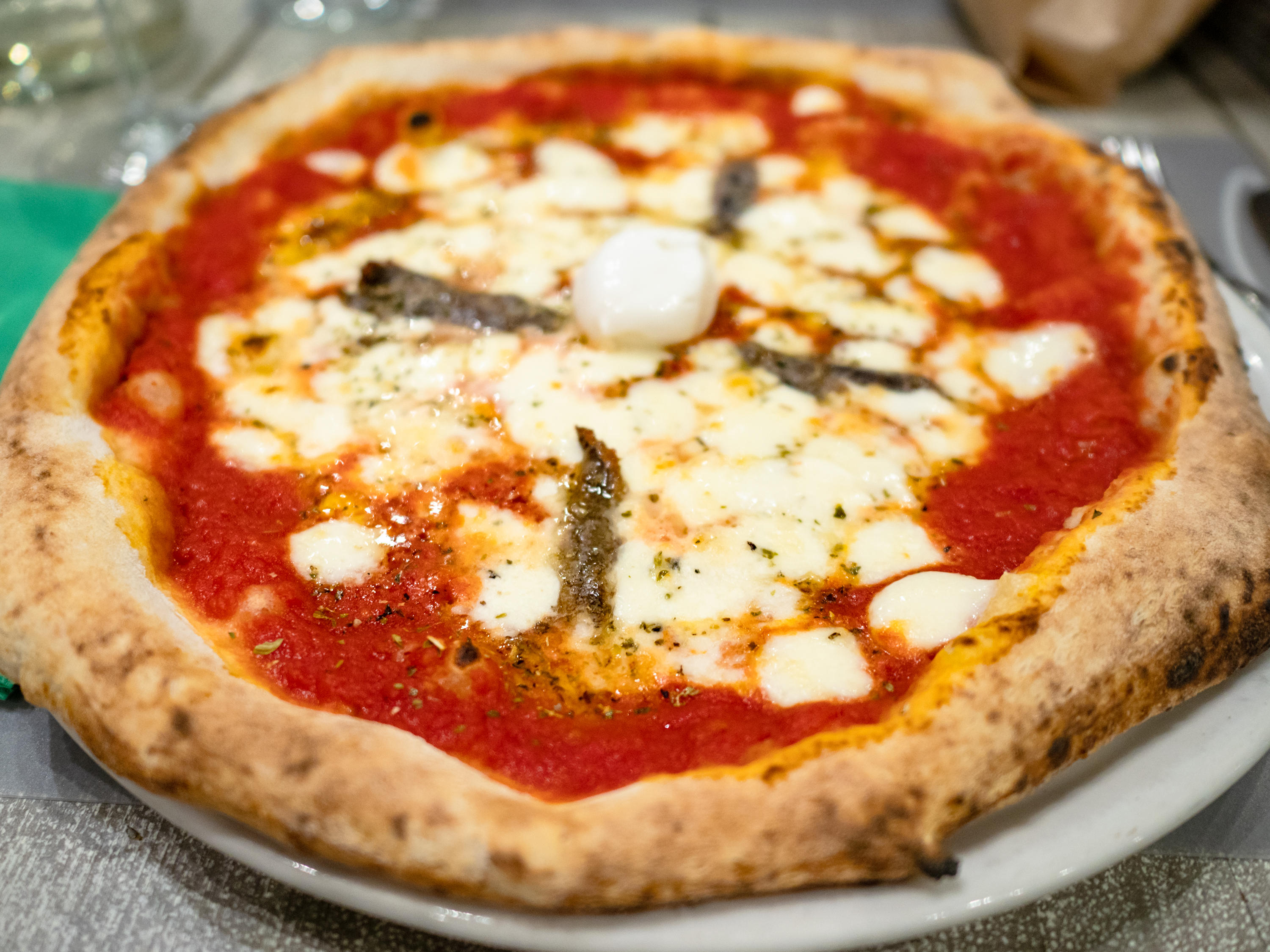 typical italian pizza Napoli with anchovies and Mozzarella cheese baked in traditional wood-fired oven on plate in local restaurant in Lombardy